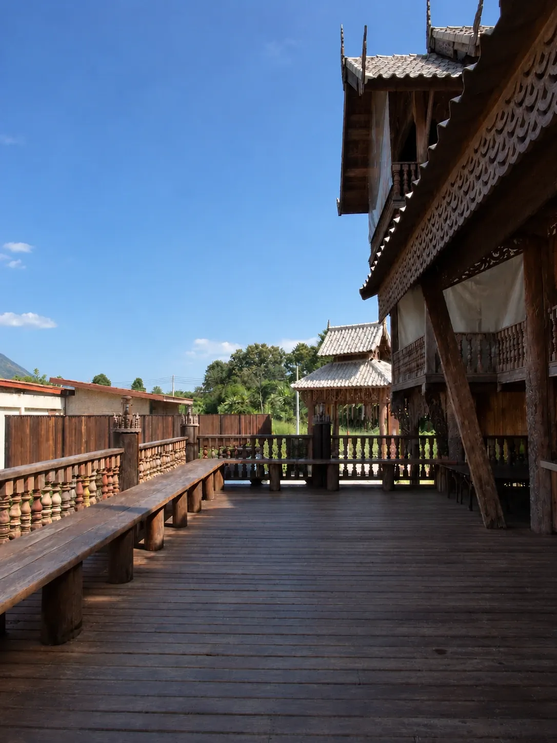Scalloped carved teak eaves and tiered roofs of the villa above the long timber veranda
