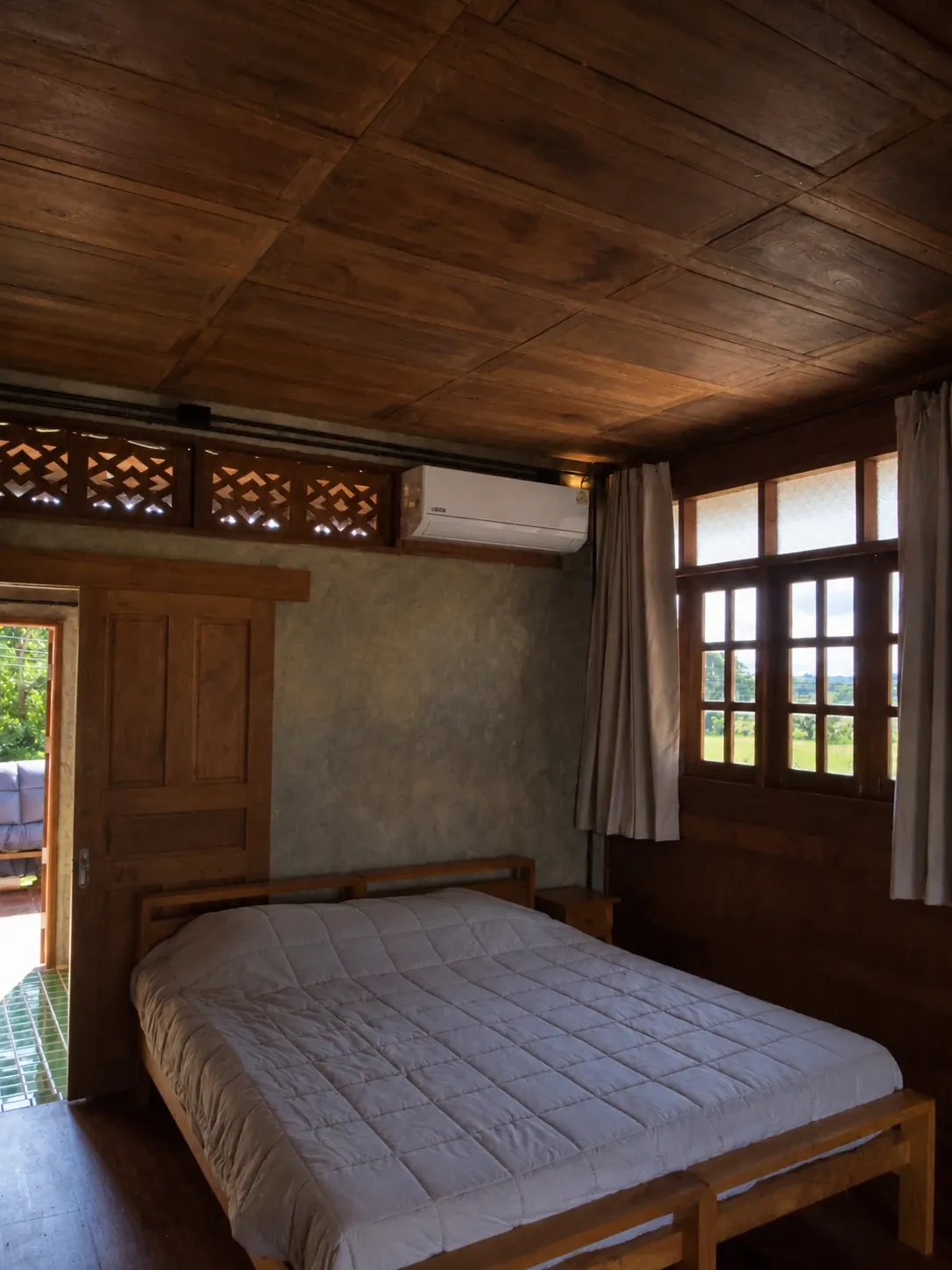 Guest bedroom with coffered teak ceiling, carved lattice transom and windows onto green fields