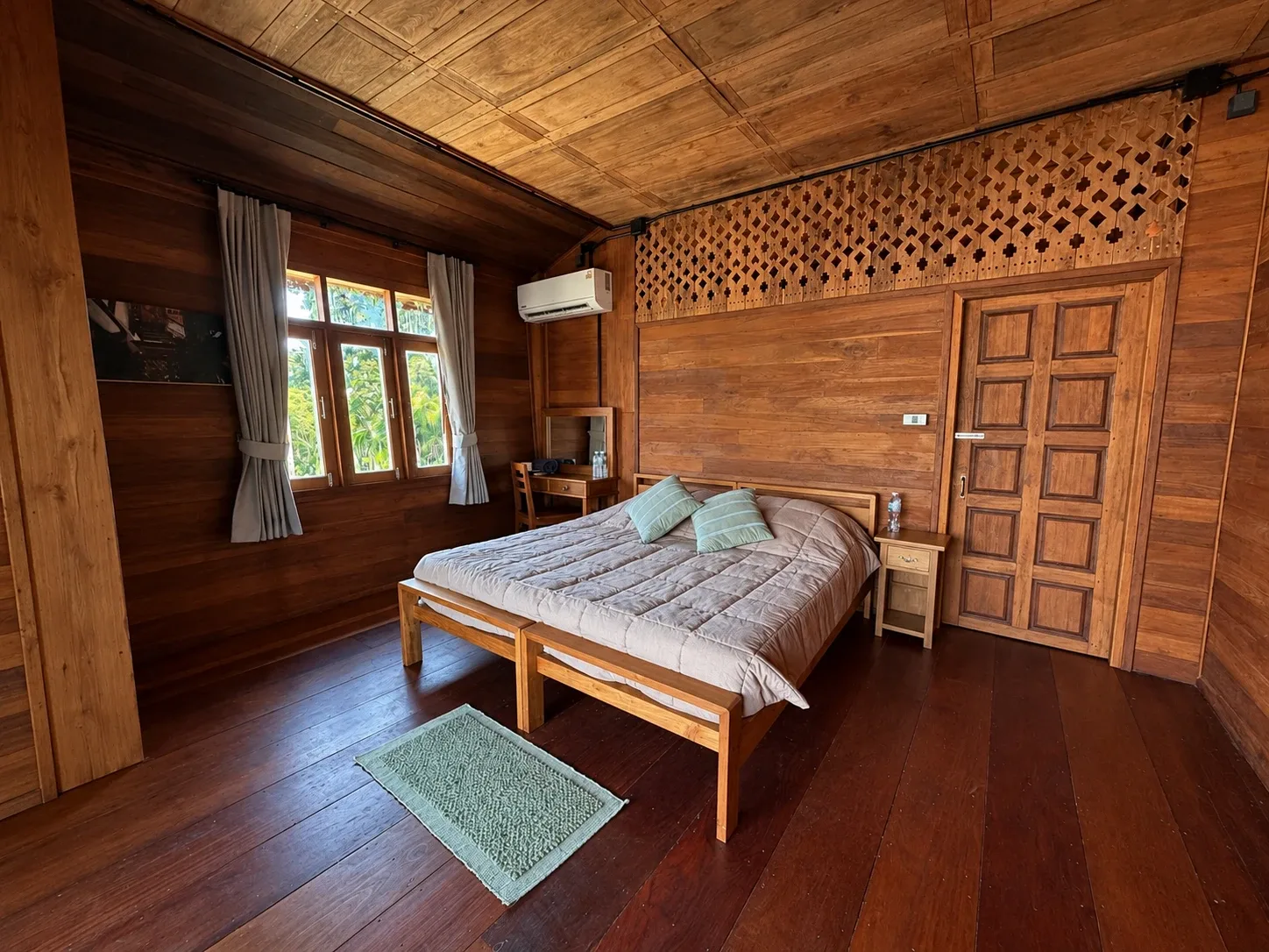 Master bedroom suite: a double bed with striped cushions under a coffered teak ceiling and a carved lattice panel above the door