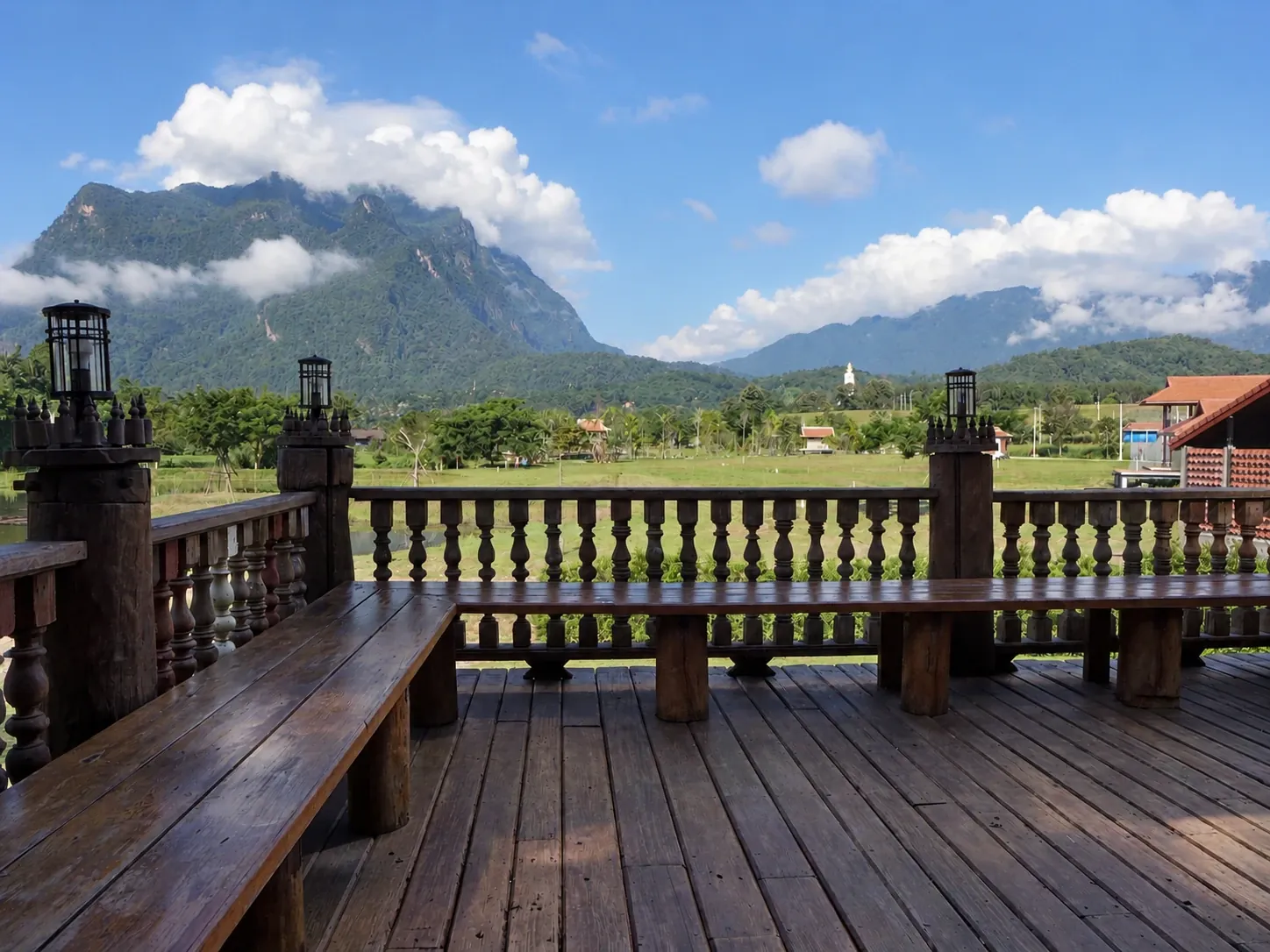 Doi Luang Chiang Dao rising above the green meadow, seen from the teak balcony with lantern posts and a built-in bench